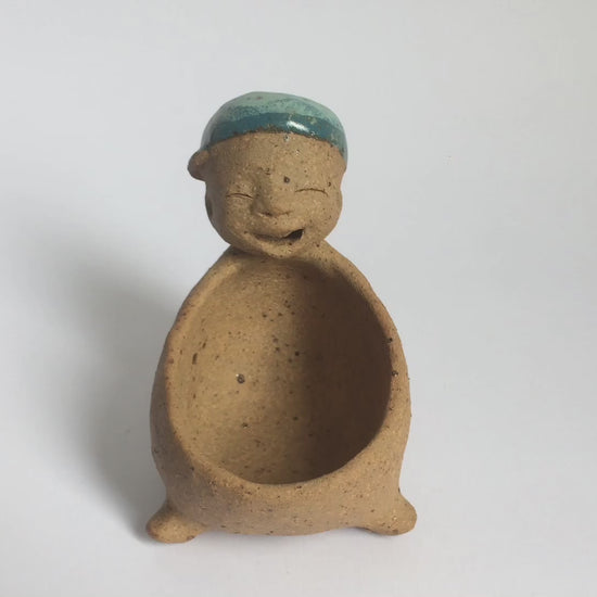 Video of brown unglazed figurative ceramic object with blue glazed accent on top