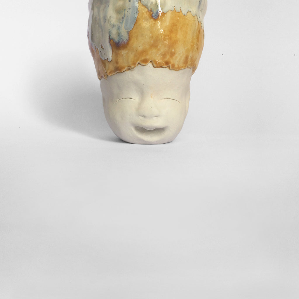 White figurative ceramic sculpture with white caramel glazed head facing front.
