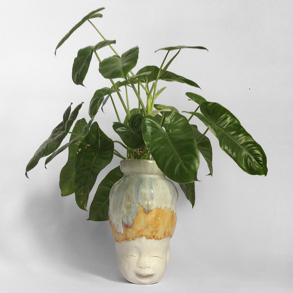 White figurative ceramic sculpture with white caramel glazed head and live plants.